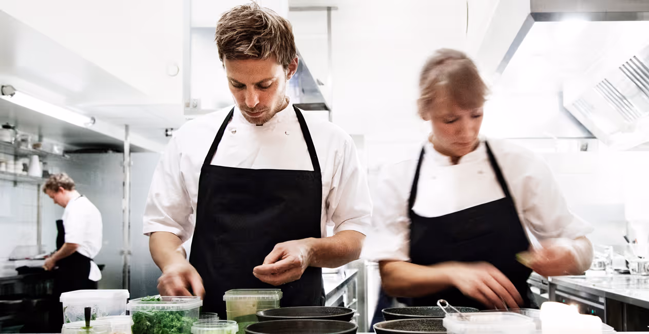 Dois cozinheiros a trabalhar numa cozinha aberta sob o teto acústico do restaurante Kadeau