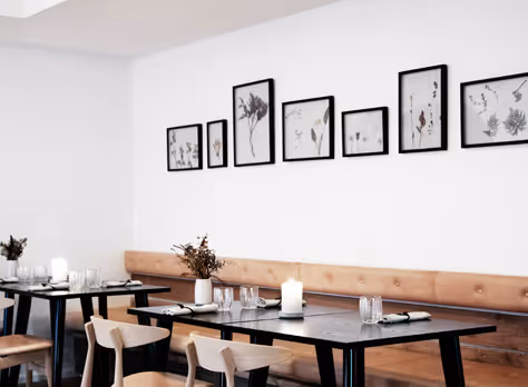 Mesas de madeira e quadros na sala do Kadeau, teto branco sem juntas