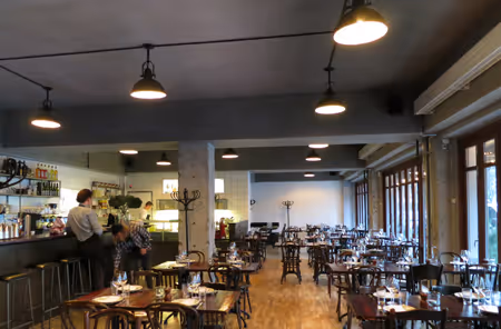 Sala do restaurante Pluto com mesas postas, candeeiros industriais e teto acústico rústico