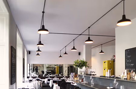 Sala do Retour Steak com candeeiros pendentes pretos e teto acústico Mute branco